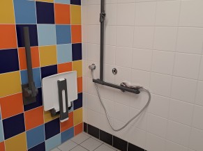 Douche adaptée avec siège, barres d'appui et douchette sur flexible (un siège de douche est aussi disponible aux douches collectives)